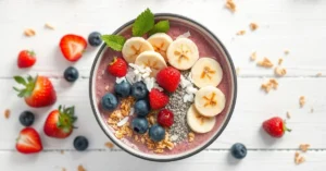 A vibrant colorful smoothie bowl with frozen mixed berries, banana slices, granola, coconut flakes, and chia seeds arranged a