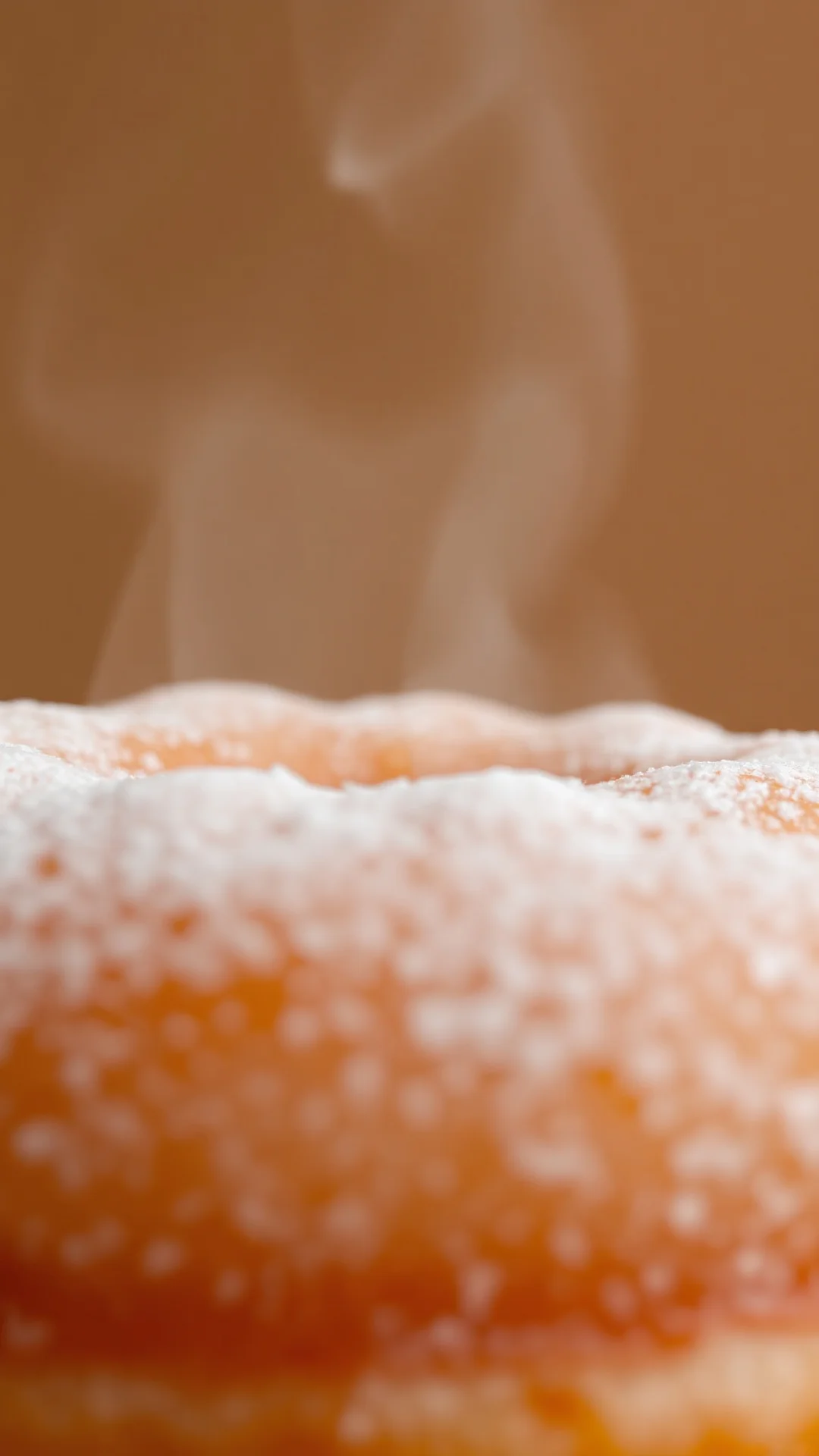 Close-up fresh fried donut with powdered sugar coating, warm golden brown surface, steam rising, soft focus background