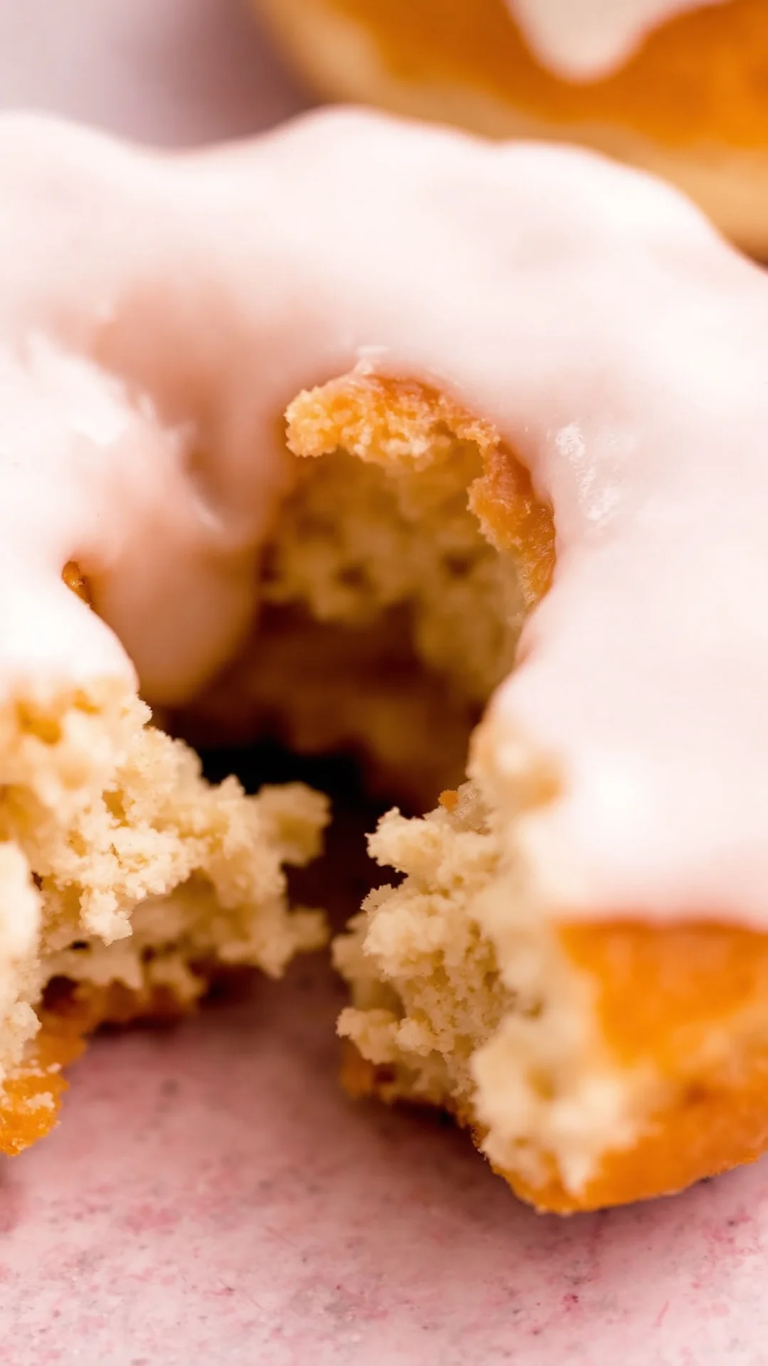 Close-up of fluffy vegan donut with glossy white icing, bite taken out showing soft moist crumb texture, pastel background